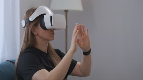 young-woman-with-HMD-display-on-head-is-viewing-photos-in-virtual-reality-gesticulating-hands-for-zooming-picture-portrait-indoors